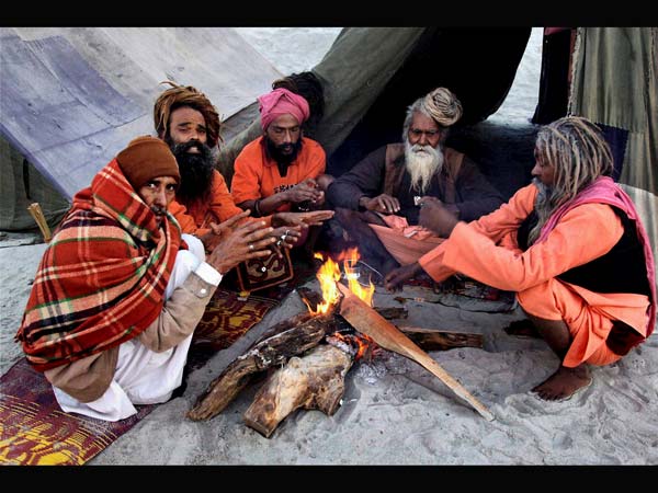 ठंड से बचने के लिए आग के पास बैठे साधु 