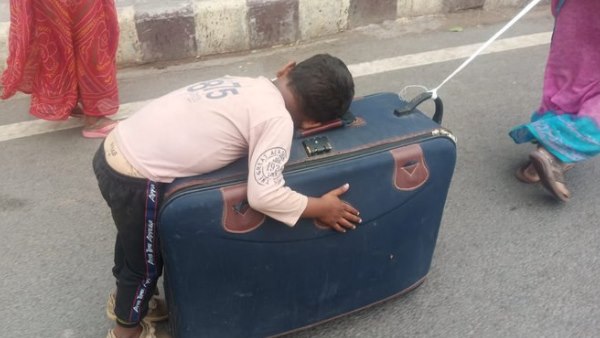सूटकेस पर सोया है बच्चा, रस्सी के सहारे खींच रही मां