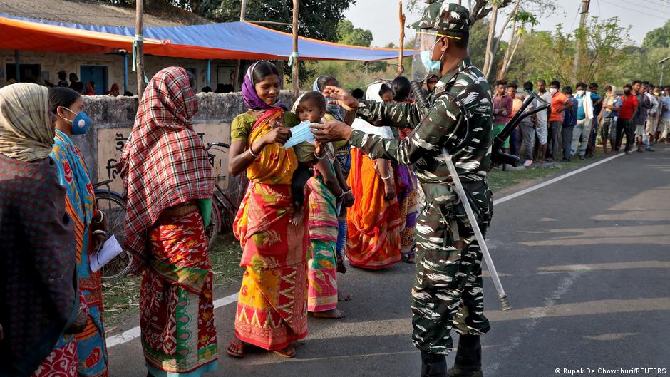 पश्चिम बंगाल में एक मतदाता को मास्क देता एक पुलिसकर्मी