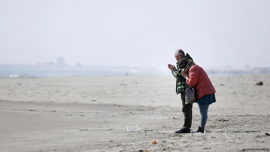 फुकुशिमा हादसे की वर्षगांठ पर समुद्र तट पर प्रार्थना करते लोग