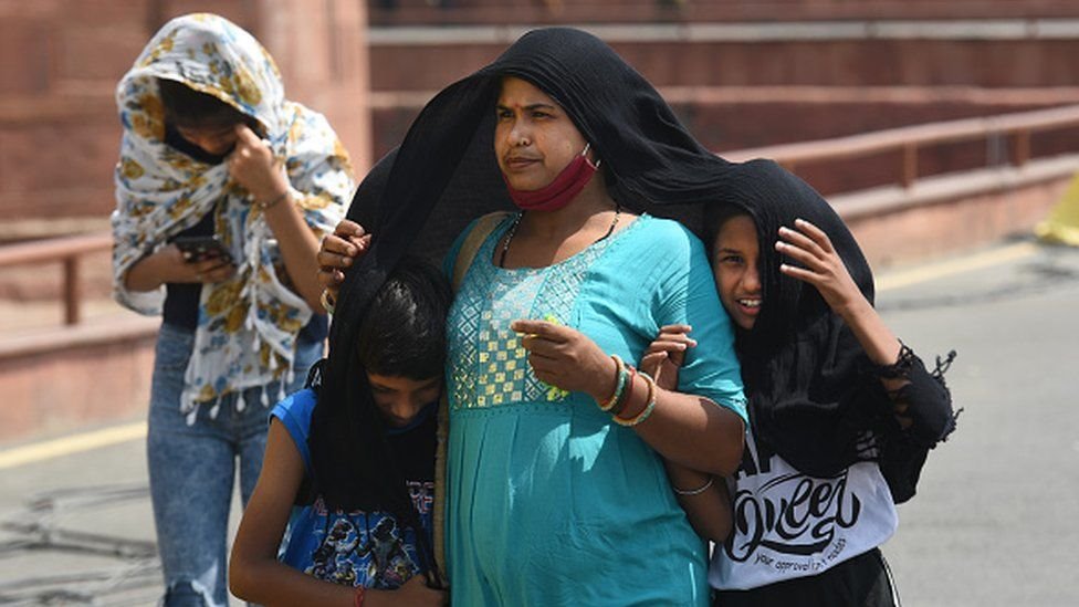 गर्मी से बचने की कोशिश में सिर ढककर चलती महिला और बच्चे