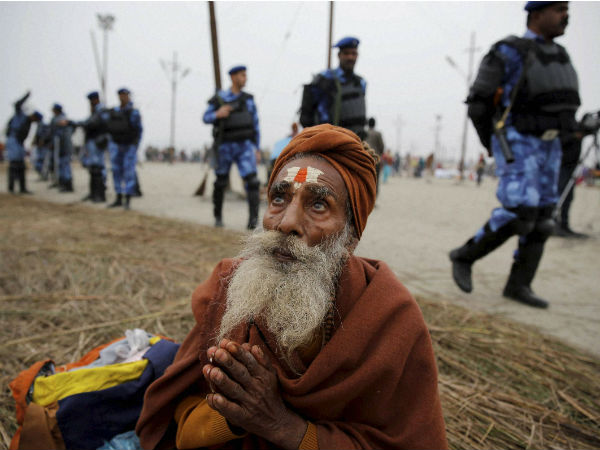 An elderly devotee prays as RAF soldiers patrol at Sangam