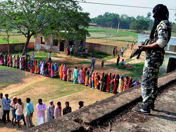 A security guard keeps vigil as voters queue up to cast their votes