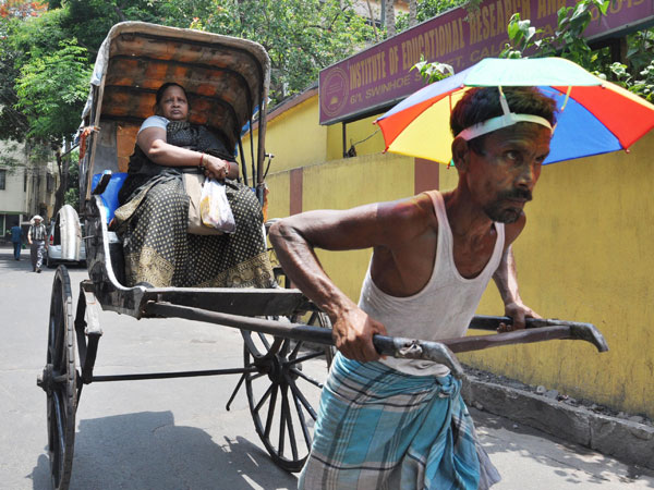 A rickshaw puller with an umbrella on a hot day in Kolkata