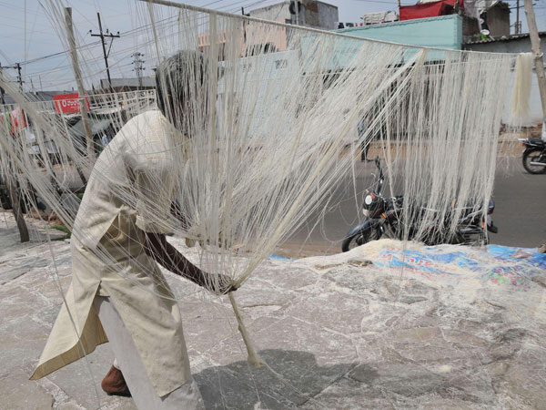 A worker hangs strands of vermicelli to dry in sun