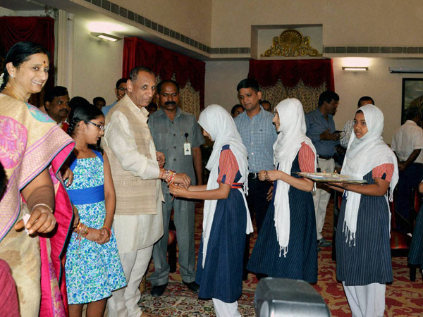 School girls in head scarf tying rakhi on Governor ESL Narasimhan