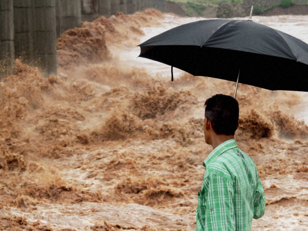 A man holding umbrella looks on as Tawi river rages