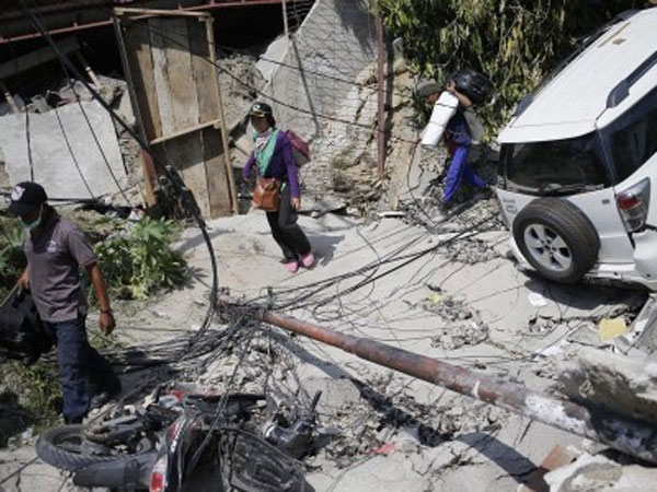 People make their way past vehicles damaged by earthquake in Palu
