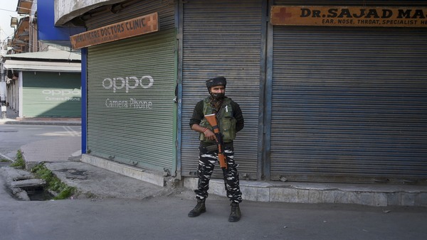 A security personnel stands guard outside closed shops during shutdown in Srinagar