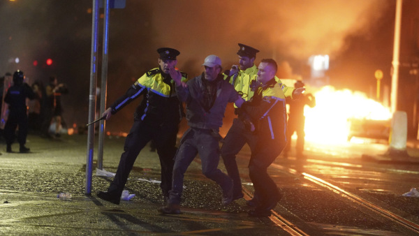 Irish police officers apprehend a man after a demonstration near the scene of an attack in Dublin city center