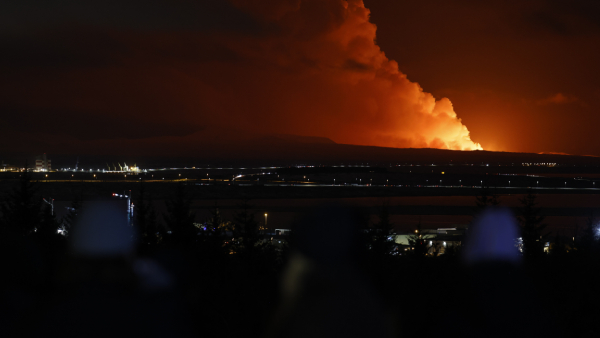 People watch as the night sky is illuminated caused by the eruption of a volcano on the Reykjanes peninsula of south-west Iceland seen from the capital city of Reykjavik