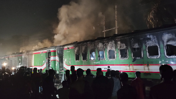 People stand near a burning passenger train at Gopibagh in Dhaka, Bangladesh