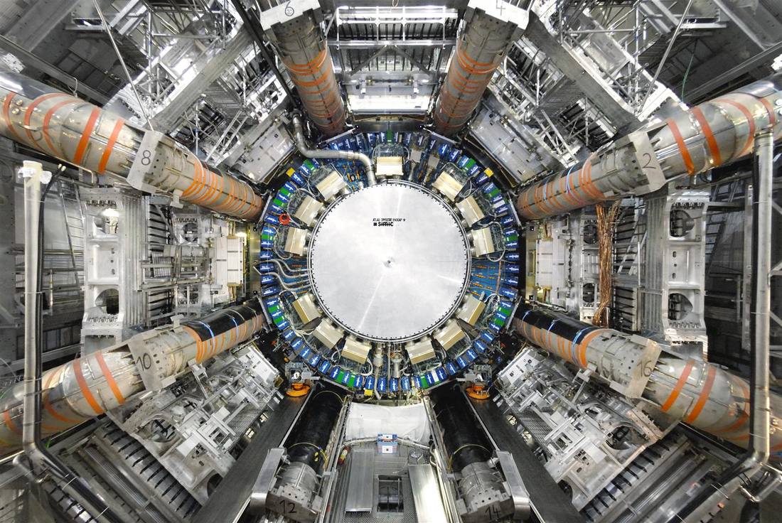 Head-on view of the ATLAS detector s giant circular end-cap inside its cavern surrounded by orange and grey support structures Head-on view of the ATLAS detector s giant circular end-cap inside its cavern surrounded by orange and grey support structures