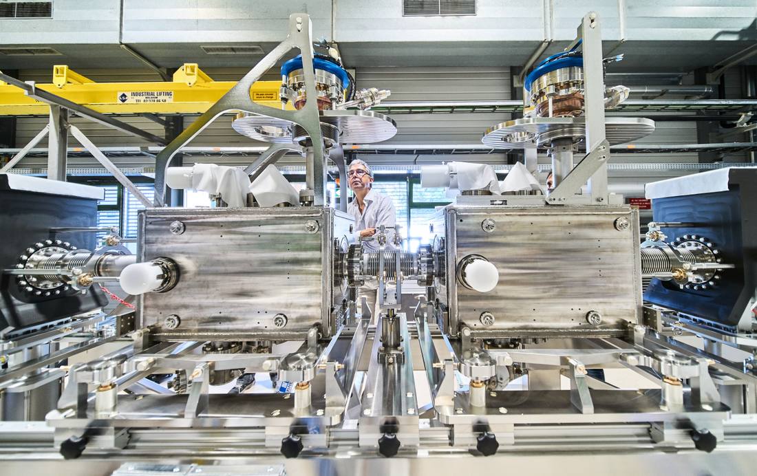 An engineer inspecting two large superconducting magnet modules side by side in a CERN assembly hall An engineer inspecting two large superconducting magnet modules side by side in a CERN assembly hall