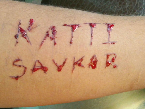 Young man writes name of Umesh Katti on hands with blade