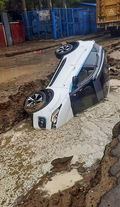 A vehicle lies in a pit after heavy rains washed away a road, in New Delhi.