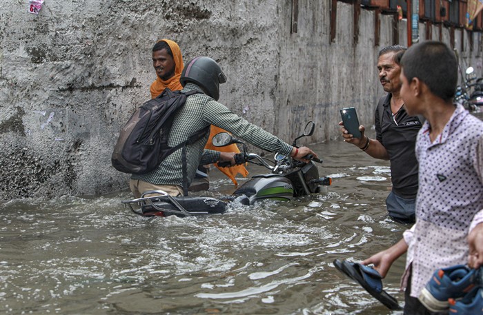 People wade through a waterlogged road near Sarai Kale Khan area after rain, in New Delhi.