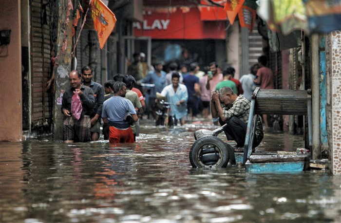 People wade through a waterlogged road near Sarai Kale Khan area after rain, in New Delhi