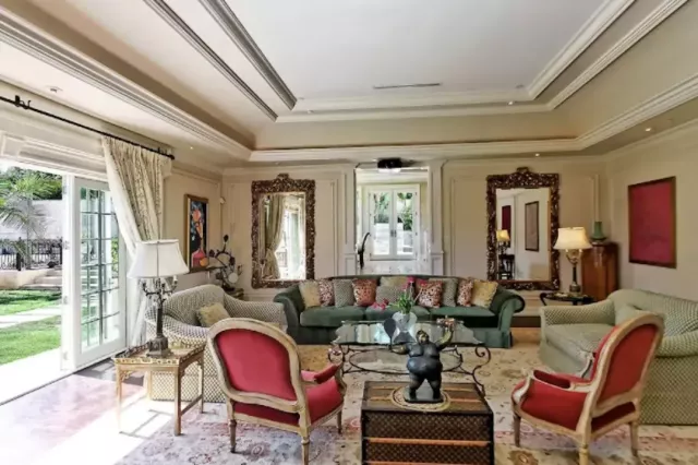 a bookshelf with a beautiful painting, and various luxurious items such as large mirrors and a grand chandelier.