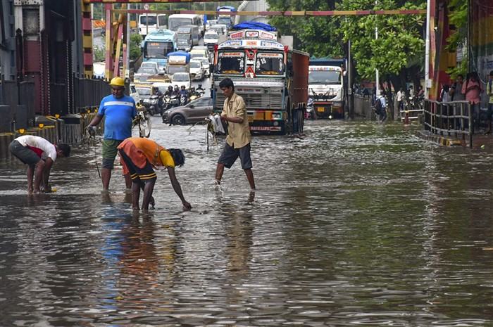 Workers clear a waterlogged road as vehicles make their way following rains, in Mumbai.