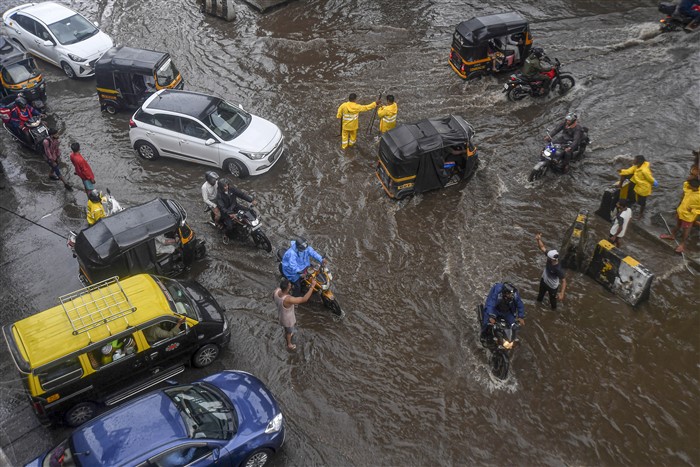 Commuters wade through a waterlogged street following rains, in Mumbai.