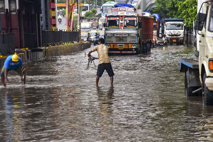 Workers clear a waterlogged road as vehicles make their way following rains, in Mumbai.