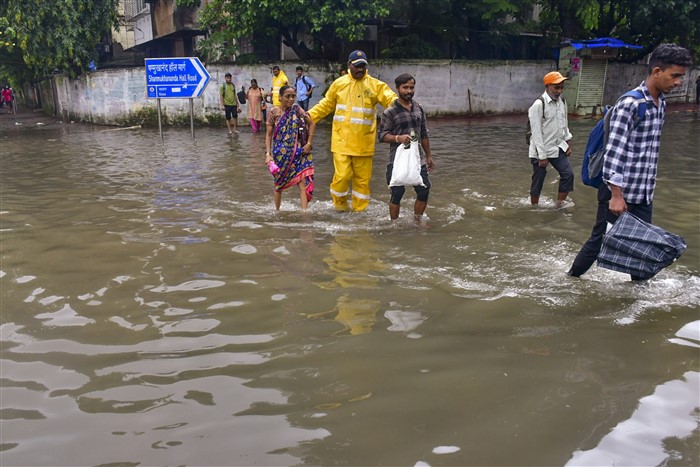 Disaster response force personnel help pedestrians to cross a waterlogged street following rains, in Mumbai.