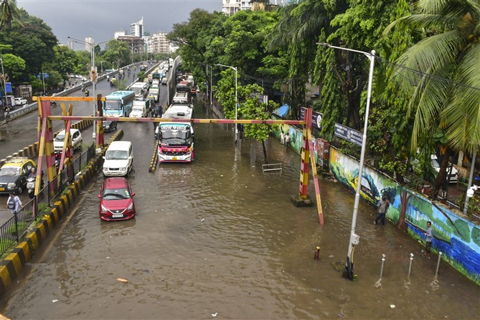 Commuters wade through a waterlogged street following rains, in Mumbai.