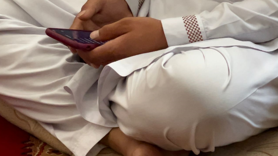 Mohammad seated on the floor scrolling through his phone